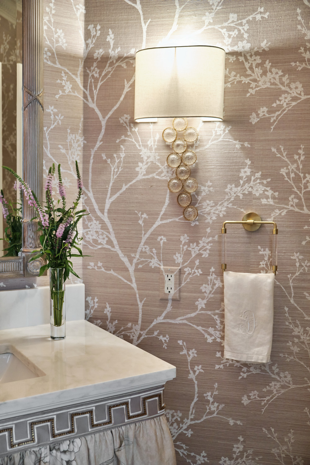 beige and brown patterned wallpaper with a gold sconce next to the bathroom vanity